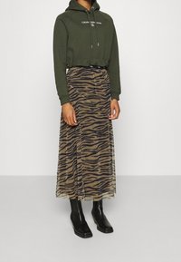 Grön kortärmad hoodie med logotyp, matchad med en genomskinlig brun kjol med zebramönster. Svarta knähöga stövlar fulländar outfiten.