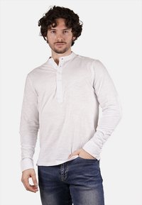 Camicia henley bianca a maniche lunghe con finitura testurizzata, dotata di una patta con bottoni e polsini aderenti, abbinata a jeans blu scuro.