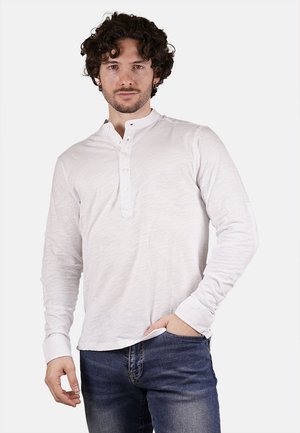 Camicia henley bianca a maniche lunghe con finitura testurizzata, dotata di una patta con bottoni e polsini aderenti, abbinata a jeans blu scuro.