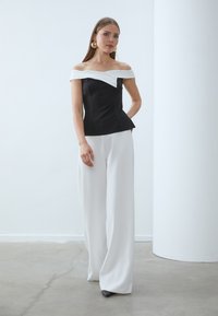Čierny a biely top bez ramienok s peplum lemom, skombinovaný s voľnými bielymi nohavicami. Hladká tkanina a štruktúrovaný dizajn. Zlato-kruhové náušnice.