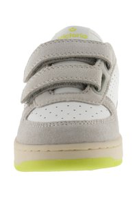 Zapatilla gris y blanca con tiras de velcro, parte superior de gamuza, puntera perforada, suela beige y acento de suela exterior en amarillo neón.