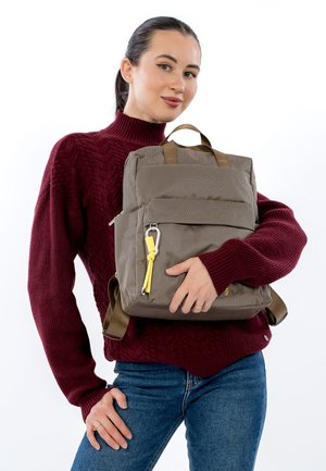 Zaino marrone con texture, con due manici superiori, spallacci regolabili e cursore della cerniera giallo. Presentato davanti a uno sfondo bianco uniforme.