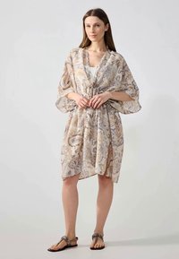 Kaftan léger à motifs en beige et couleurs pastel douces. Dispose de manches fluides, d'une taille nouée et d'une coupe décontractée. Tissu texturé.