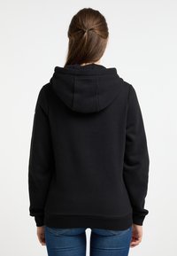 Fekete kapucnis pullover, puha textúrával, laza fazonnal és bordás mandzsettákkal. Tágas kapucnival és varrás nélküli hátrésznél tervezték.