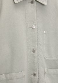 Vaaleanvihreä nappikauluspaita, jossa on teksturoitu kangas, hopeanväriset napit, laskostettu kaulus ja kaksi etutaskua.