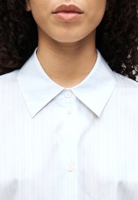 Camicia a maniche lunghe azzurra a righe con colletto classico e due bottoni al collo. Tessuto liscio con sottili linee verticali.