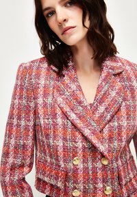 Roze en oranje tweed blazer met een dubbele sluiting aan de voorkant, gouden knopen en een gestructureerde stof, met een notch lapel en een gestructureerde pasvorm.