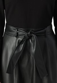 Falda de cuero sintético negro con una cinturilla ancha y un detalle de cinturón anudado, textura suave y costuras sutiles alrededor de la cintura.