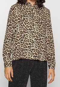 Chemise à boutons en imprimé léopard beige, dotée de manches longues, d'un col et d'une coupe ample, fabriquée en tissu léger.