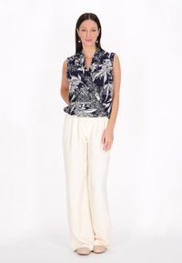 Blusa sin mangas de color marinero con patrón floral blanco; diseño drapeado. Combinada con pantalones de pierna ancha en color crema y zapatos beige. Textura de tela suave.
