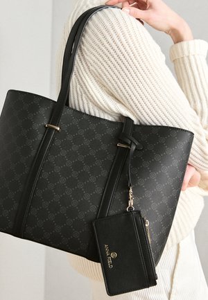 Sac cabas noir avec motif logo, surface texturée, accents dorés et bretelles ajustables. Comprend un porte-cartes noir amovible.