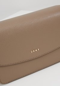Pochette DKNY en cuir marron avec surface texturée et logo doré sur le rabat avant.