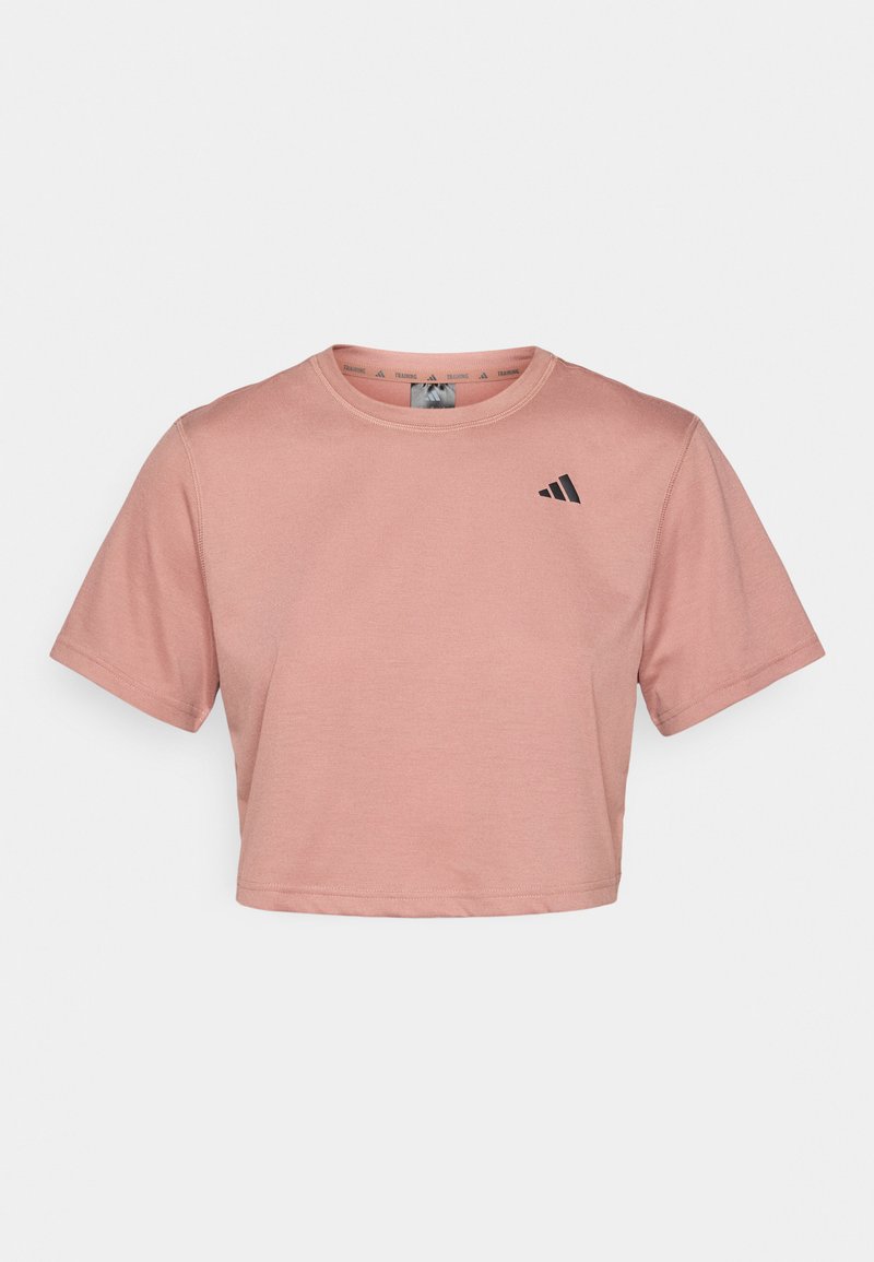 Camiseta corta de manga corta en suave algodón rosa claro con cuello redondo y acento de logo negro en el lado izquierdo del pecho. Textura suave, diseño sencillo.