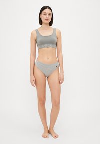 Sivá bavlnená športová podprsenka s nápisom "POLO" a zodpovedajúcimi sivými vysokými nohavičkami s malým logom. Hladká textúra, voľný strih.