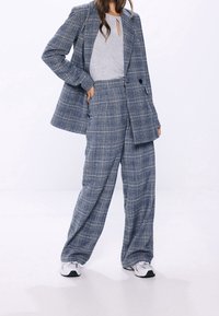 Camiseta gris jaspeado bajo un blazer azul a cuadros y pantalones de pierna ancha, con un ajuste holgado y textura suave, combinados con zapatillas.