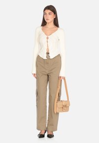 Top bianco a coste con maniche lunghe, scollatura a V e dettagli con bottoni, abbinato a pantaloni cargo beige e una borsa a tracolla intrecciata beige. Scarpe nere a punta.
