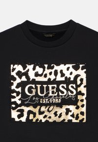 Černá mikina s kulatým výstřihem, s metalickým zlatým designem potisku leopardího vzoru a textem "GUESS Los Angeles EST. 1983" na přední straně.