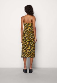 Blommig midiklänning med tunna band, med en svart bakgrund och gula samt gröna blommönster. Bärs med svarta klackiga skor.