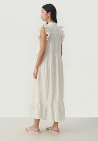 Robe maxi couleur crème avec des manches à volants, en tissu texturé et à ourlet en cascade. Présente une coupe décontractée et tombe en dessous de la cheville.