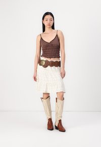 Crop top élastiqué marron, jupe blanche à volants, ceinture décorative marron et bottes de cowboy beige avec des accents crème. Design simple et superposé.
