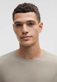 Tricou gri deschis, cu mâneci scurte și guler rotund. Textură netedă, design aderent, cusături minime și o siluetă curată.