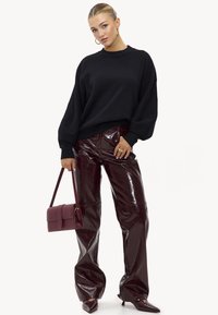 Pull noir oversize, pantalon en simili cuir bordeaux brillant, escarpins à bout pointu et petit sac à main bordeaux avec fermeture à rabat.