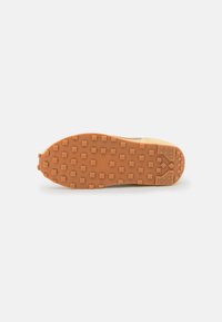 Rubber sole with a textured, raised pattern for traction. Soft upper in beige with a light tan accent, designed for comfort and durability.