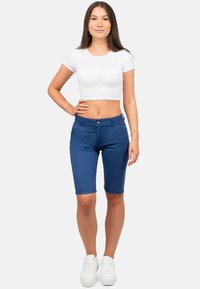 Bermuda shorts in denim blu navy con una vestibilità slim, cinque tasche e chiusura con bottone. Abbinati a un crop top bianco aderente e sneakers.