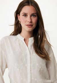 Witte geborduurde blouse met een ronde halslijn, subtiele bloemmotieven, lange mouwen en een sluiting met knopen aan de voorkant. Soepele linnen textuur.