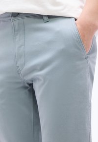 Κοντινό πλάνο ενός ατόμου που φοράει ανοιχτό μπλε παντελόνι, με το δεξί  χέρι στην μπροστινή τσέπη, και ένα λευκό πουκάμισο μερικώς ορατό.