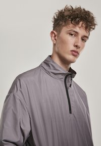 Grå letvægts pullover med høj krave og halv lynlås. Stoffet har en glat, let skinnende tekstur uden synlige mønstre.