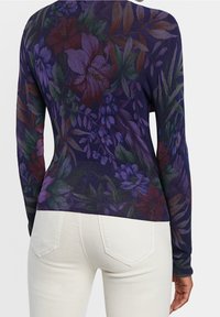 Primer plano de una persona que lleva una camiseta de manga larga ajustada con un patrón floral oscuro y unos vaqueros blancos desde atrás.