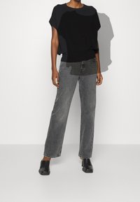 Černý oversize pletený top, šedé široké džíny a černé muly. Látky vypadají měkce; džíny mají vybledlý vzhled. Čisté linie; minimalistický styl.