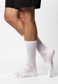 Weiße Sportsocken mit geripptem Muster, gepolsterten Bereichen und Mesh-Akzenten für Atmungsaktivität. Mit verstärkten Fersen- und Zehenbereichen.