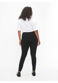Crne skinny traperice s stražnjim džepovima, uparene s bijelim majicom s kratkim rukavima. Tkanina ima glatku teksturu, usko se prilagođavajući tijelu.