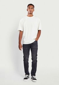 Vit oversized t-shirt med korta ärmar, kombinerad med mörka jeans i denim. Svarta och vita sneakers med kontrasterande ränder och snören.