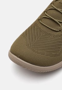 Grüner Textil-Sportschuh mit einem atmungsaktiven Mesh-Obermaterial, das eine strukturierte Oberfläche, eine abgerundete Zehenpartie und eine leichte Gummisohle aufweist.