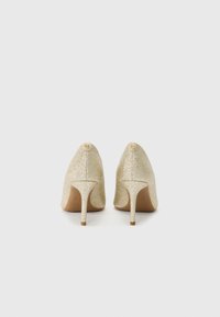 Gold glitter high-heeled shoes with a pointed toe design. Features a thin stiletto heel and a small logo accent on the back.