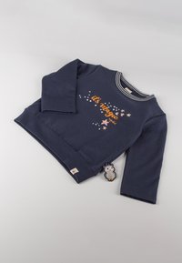 Felpa blu navy con maniche lunghe, colletto a righe bianco e grigio, e testo stampato "è magia" con stelle. Include un'etichetta a forma di pinguino.