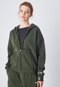 Grüne Zip-Hoodie aus weichem Baumwollmaterial mit einem Logo-Druck auf der Vorderseite. Verfügt über eine Kapuze, Kängurutaschen und detaillierte Bündchen.