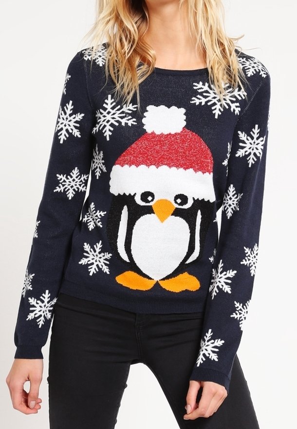 Modellen bär en marinblå tröja med en stor pingvin som har en röd hatt och snöflingemönster, tillsammans med svarta jeans.