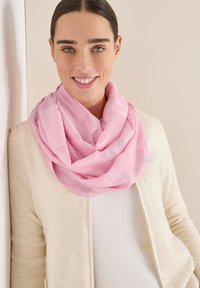 Lys pink uendelighedsscarf med et tekstureret mønster og en subtil glans, båret over en cremegul sweater, mod en neutral baggrund.