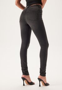 Czarne skinny jeans o gładkiej teksturze, wysoki stan, dwa tylne kieszenie, w połączeniu z czarnymi sandałami na obcasie.