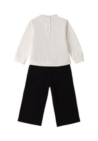Biała bluzka z długim rękawem i zapięciem na guziki z tyłu, w połączeniu z czarnymi spodniami o szerokich nogawkach. Miękka tkanina z minimalnymi detalami.