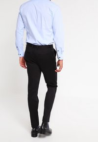 Ljusblå långärmad skjorta med knappmanschetter, kombinerad med svarta byxor och svarta ankelstövlar. Klädseln har en smal passform och slät yta.