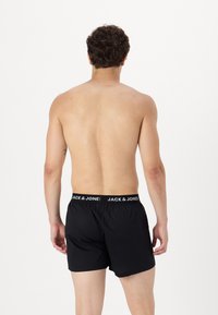Črne bokserice z elastičnim pasom z belim logotipom "JACK & JONES". Model je prikazan s hrbta, brez majice.