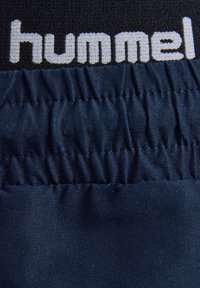 Elastischer Bund mit dunkelblauem Stoff unten und strukturiertem schwarzem Stoff mit weißem "hummel"-Schriftzug oben.