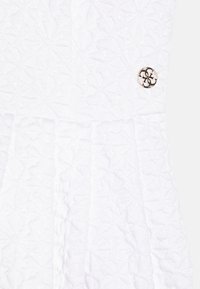 Biała sukienka z teksturowanej tkaniny z geometrycznym wzorem, z widocznym okrągłym przyciskiem z logo w okolicy talii.