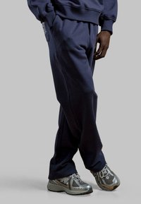 Marineblauwe trainingsbroek van zacht materiaal met zijzakken, gecombineerd met grijze New Balance sneakers met een bovenkant van mesh en een gestructureerde zool.