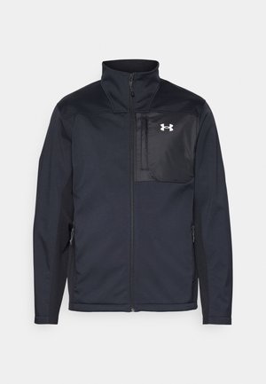 Veste noire à manches longues avec un col montant, dotée d'un zip avant, de poches latérales et d'un panneau central noir contrastant avec un logo.